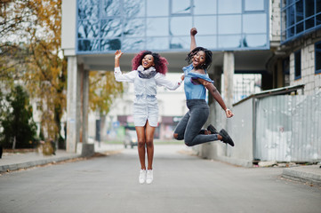 Two attractive african american womans jumping against modern multistory building.