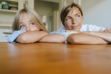Mother and daughter leaning on kitchen table at home
