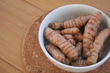 Turmeric rhizome in a bowl on wooden table. Curcuma longa with selective focus
