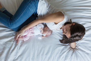 young mother lying on bed at home with her baby girl. family and love concept
