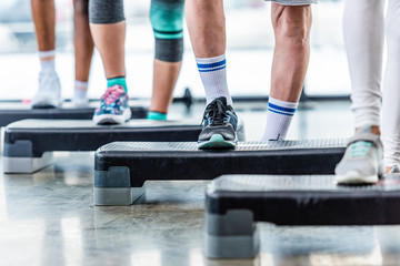 partial view of sportspeople doing exercise on step platforms at gym