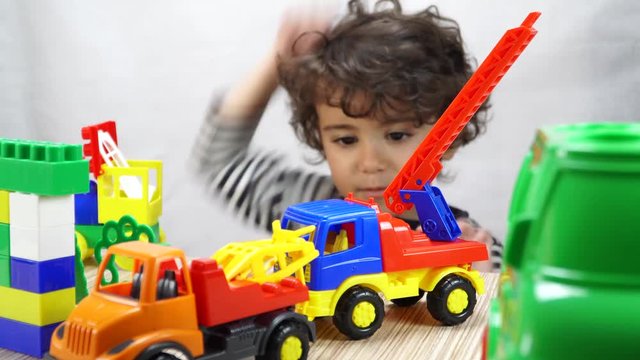 Little cute boy playing with colorful plastic cars. Colorful plastic tow car and fire truck. 4K