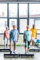Fototapeta na wymiar happy multicultural senior athletes synchronous exercising on step platforms at gym