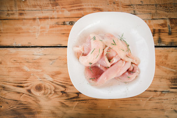 Fresh organic chicken meat on white dish with rosemary on the wooden table