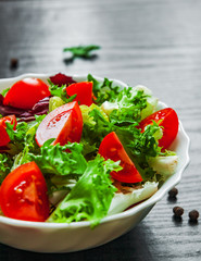 arious fresh mix salad leaves with tomato in bowl on dark wooden background