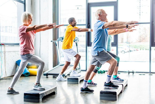 side view of multicultural senior athletes synchronous exercising on step platforms at gym