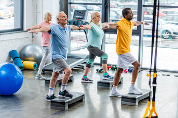 selective focus of senior multicultural athletes synchronous exercising on step platforms at gym