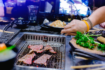 Selective focus to the woman's hand is grilling wagyu beef in Japanese grilled restaurant