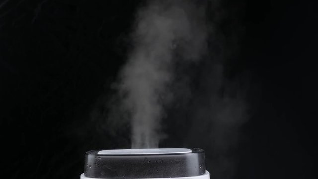 Mist from a black electric humidifier & oil diffuser in a dark room
