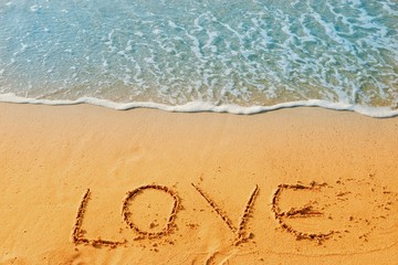 Valentine's Day concept, the word love writing on sand beach with blue waves ocean.