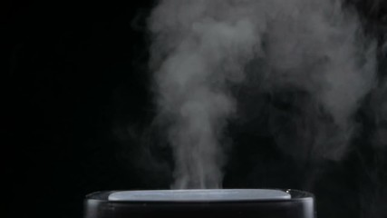 Mist from a black electric humidifier & oil diffuser in a dark room