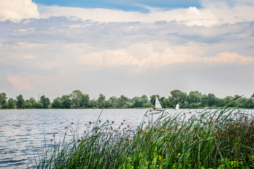 beautiful blue sky with white clouds over river, a small sailboat passes.