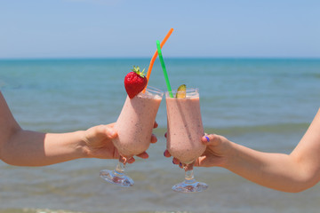 two female hands are holding strawberry milkshakes on the background of the sea