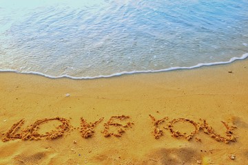 Valentine's Day concept, the word love you writing on sand beach with blue waves ocean.