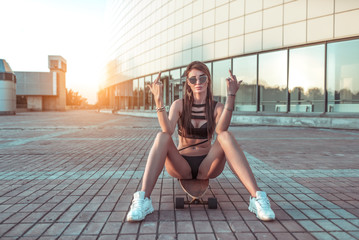 Beautiful girl sitting on a skateboard. The gesture of the hand shows middle finger. The concept of...