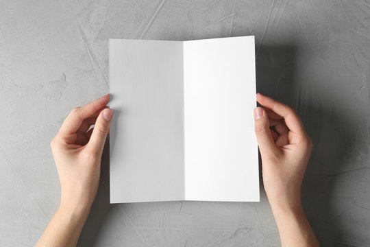 Woman holding blank brochure mock up on light background, top view