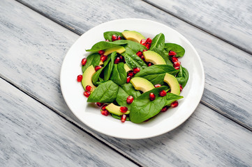 Avocado salad with baby spinach and pomegranate on a white plate on a wooden table