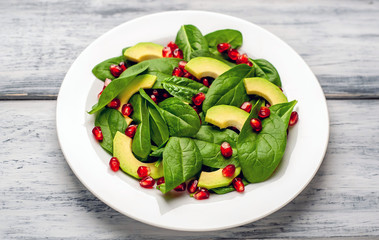 Avocado salad with baby spinach and pomegranate on a white plate on a wooden table
