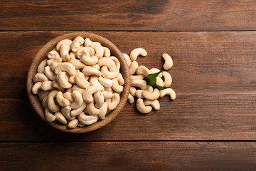 Tasty cashew nuts in bowl on wooden table, top view. Space for text