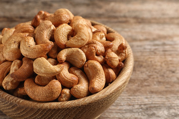 Tasty cashew nuts in bowl on wooden table, closeup. Space for text
