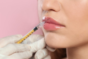 Young woman getting lips injection on color background, closeup. Cosmetic surgery