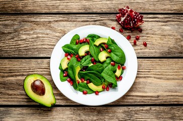 Avocado salad with baby spinach and pomegranate on a white plate on a wooden table