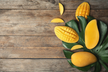 Flat lay composition with mango and tropical leaf on wooden background. Space for text