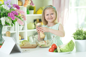 Cute little girl spicing  salad on kitchen table