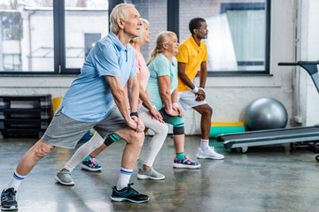 side view of senior multiethnic athletes synchronous stretching at gym