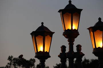 Fototapeta na wymiar Three lamps, lit, silhouetted against a dusky evening sky, with foliage in the background