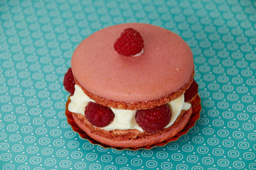 big pink macaroon with raspberry round cake on blue background