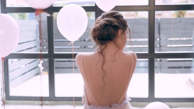 innocent girl stands in a dress in pink and purple hues with an open bare back and shoulders, a fragile and attractive figure with healthy and delicate skin, dark curls neatly fall on the tender body