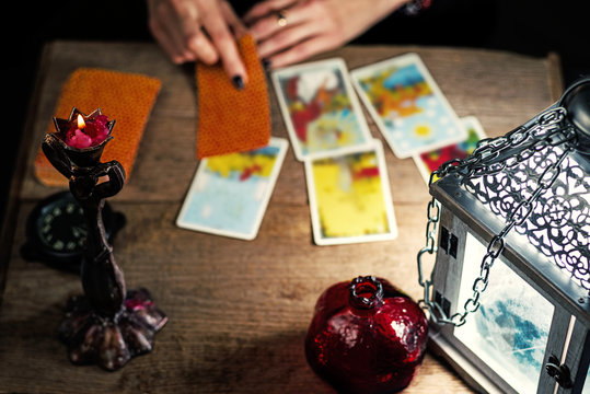 Fortune-telling on traditional tarot cards on the old wooden table with a lantern and a candle. Selective focus.