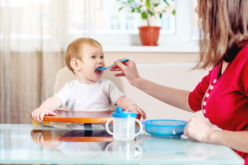 Mom feeding the baby holding out her hand with a spoon of food in the kitchen. Healthy baby food