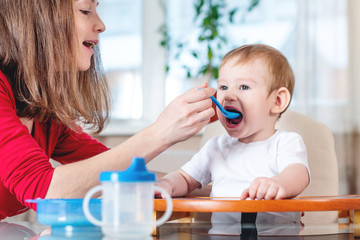 Mom feeding the baby holding hand with a spoon of porridge. Emotions of a child while eating healthy food