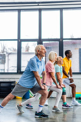 side view of senior multiethnic sportspeople synchronous stretching at sports hall