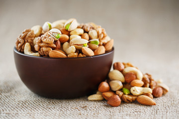 Mix of different nuts in a wooden cup against the background of fabric from burlap. Nuts as structure and background, macro. Top view.
