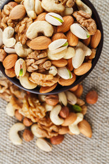 Mix of different nuts in a wooden cup against the background of fabric from burlap. Nuts as structure and background, macro. Top view.