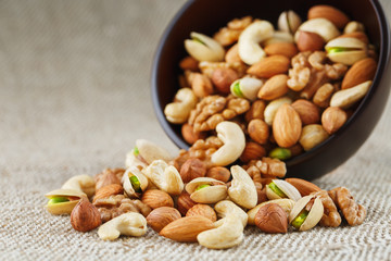 Mix of different nuts in a wooden cup against the background of fabric from burlap. Nuts as structure and background, macro. Top view.