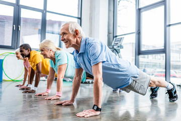 selective focus of multiethnic senior sportspeople synchronous doing plank at gym