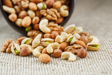 Mix of different nuts in a wooden cup against the background of fabric from burlap. Nuts as structure and background, macro. Top view.