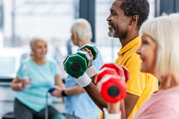 selective focus of interracial mature couple doing exercise with dumbbells at gym - Powered by Adobe