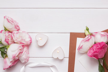Flowers, heart shaped candles and paper envelopes on the white wooden background.