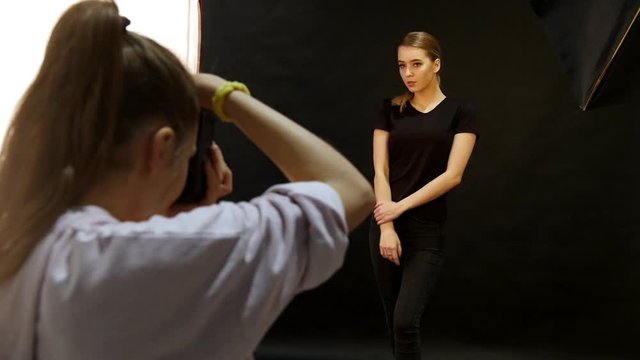 Young woman model having a photo session in the studio. Shooting the model in black clothes. The photographer uses flash