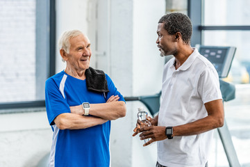 multicultural mature sportsmen talking to each other during rest at gym