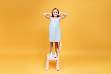 Little girl is standing on the chair and showing strong arms