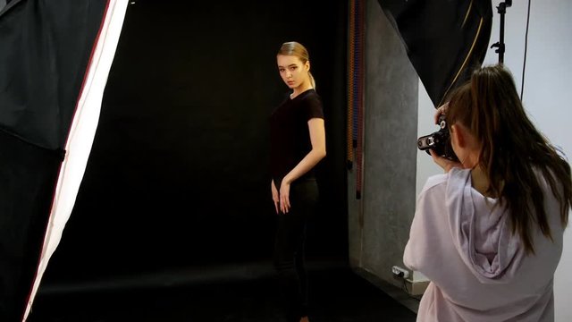 Young woman model having a photo session in the studio. Shooting the model in black clothes. The model poses differently. Shooting in full height