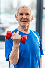 Fototapeta na wymiar smiling senior sportsman exercising with dumbbell at gym