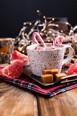 Cocoa with marshmallows in a white mug, different Christmas candies and sweets on a wooden background. Photo in dark style and free space for text. Candles and holiday decorations. 