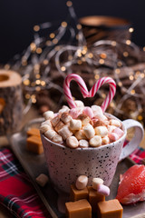 Cocoa with marshmallows in a white mug, different Christmas candies and sweets. Photo in dark style and free space for text. Candles and holiday decorations. Postcard and greetings.